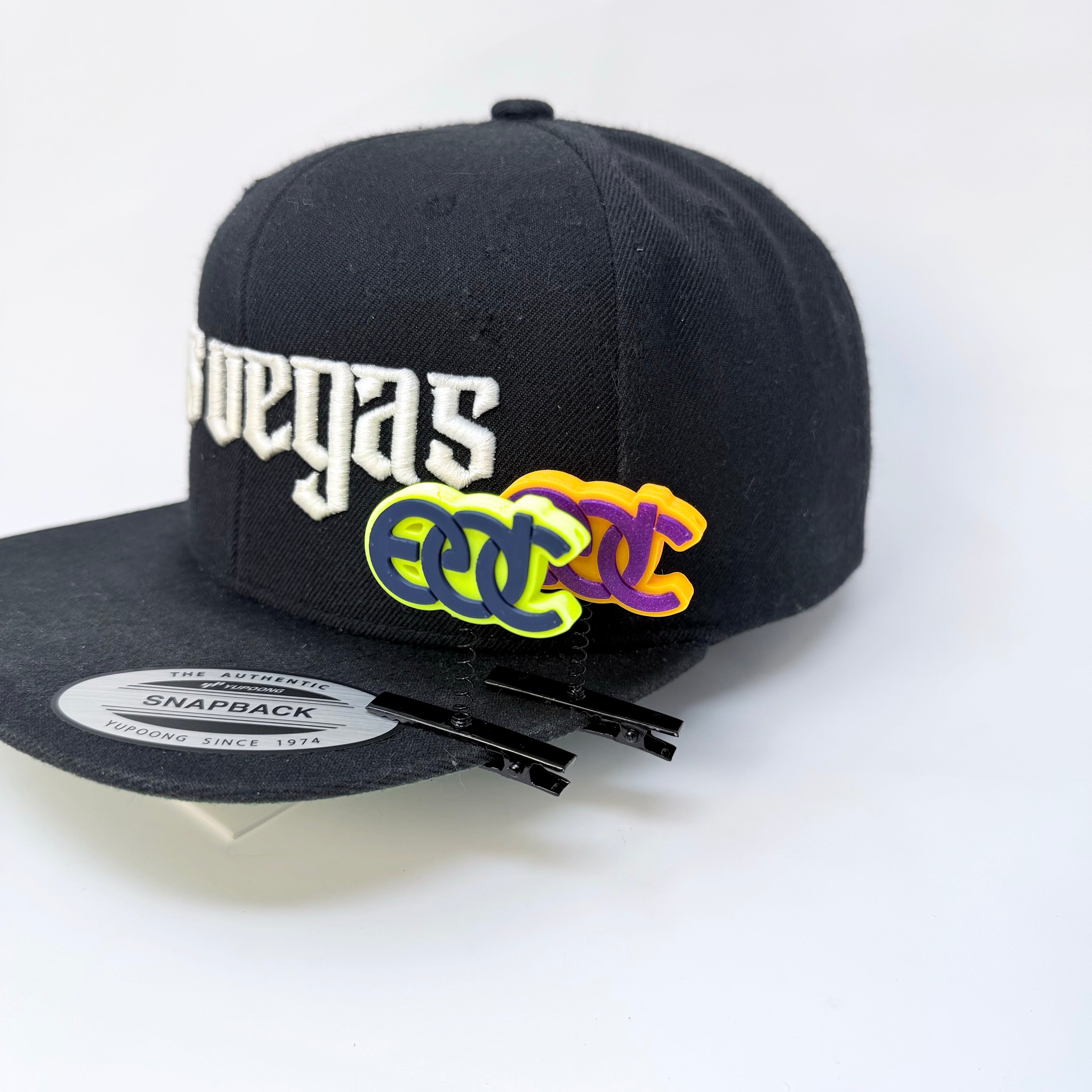 Two EDC rave sprout spring clips in orange purple and neon yellow turquoise colors on a black flat-bill hat with white Las Vegas text