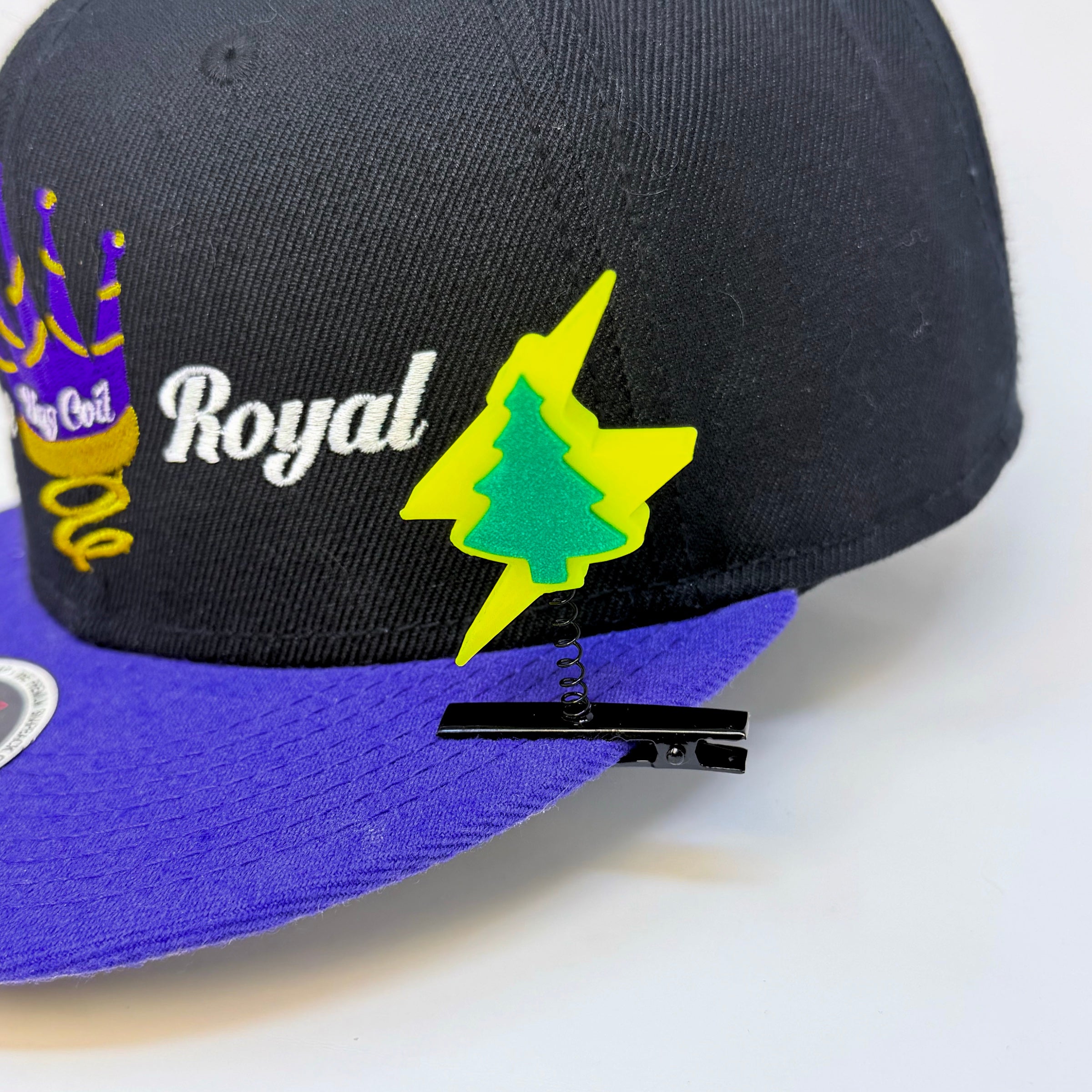 Electric Forest lightning bolt pine tree rave sprout in neon yellow and teal green clipped to the brim of a black and purple Royal snapback hat