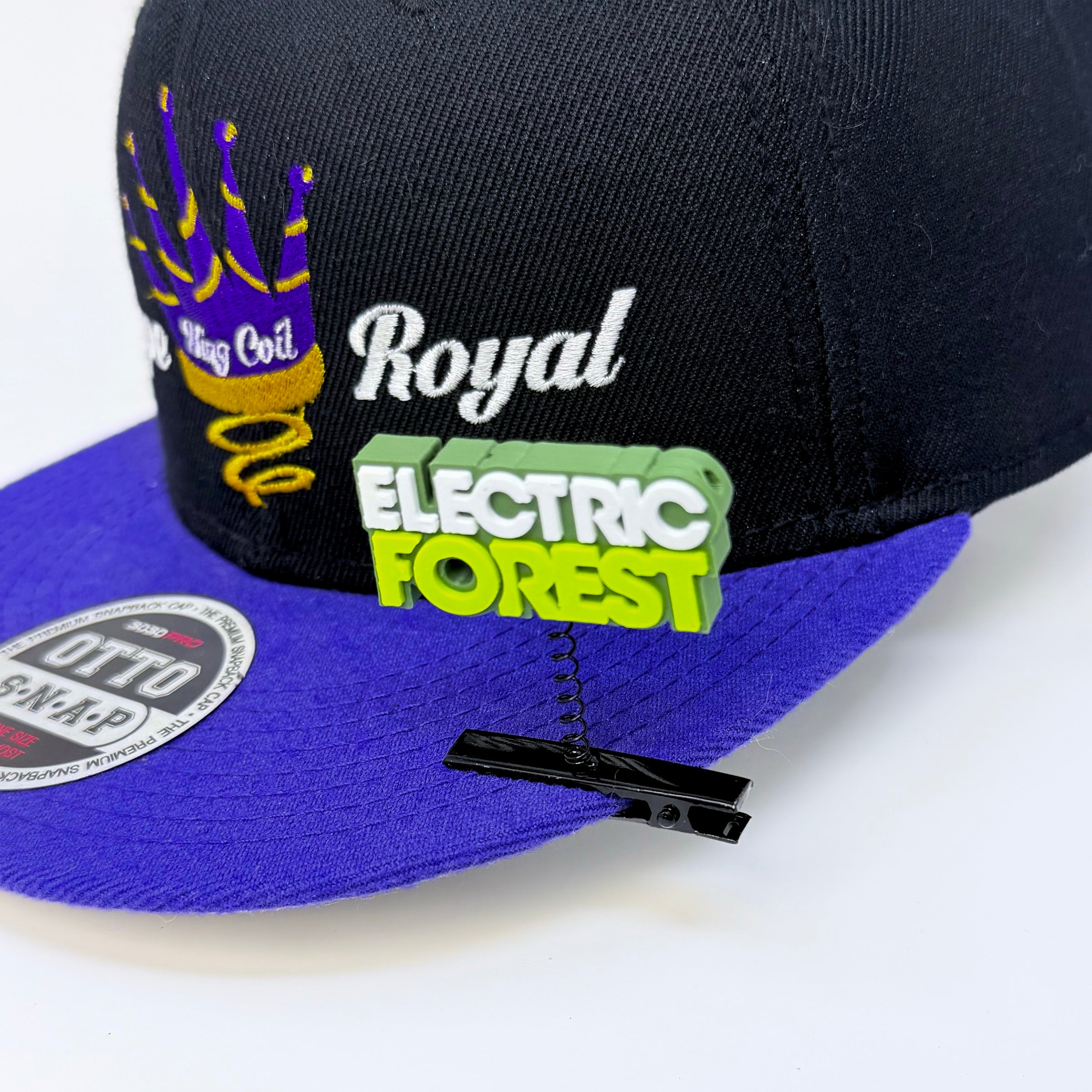 Electric Forest text rave sprout in dark green, white, and neon green clipped to the panel of a black and purple Royal snapback hat