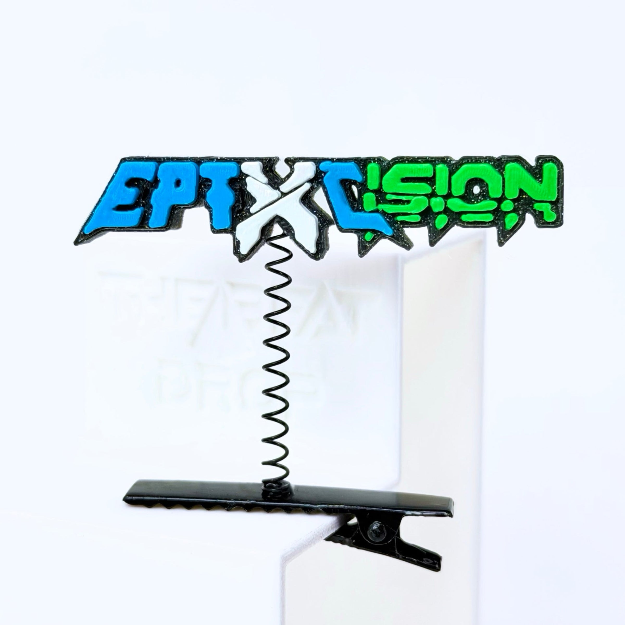 A novelty desk clip featuring Excision and Eptic in a stylized graffiti font with a black spring and black clip base, shown on a white background.