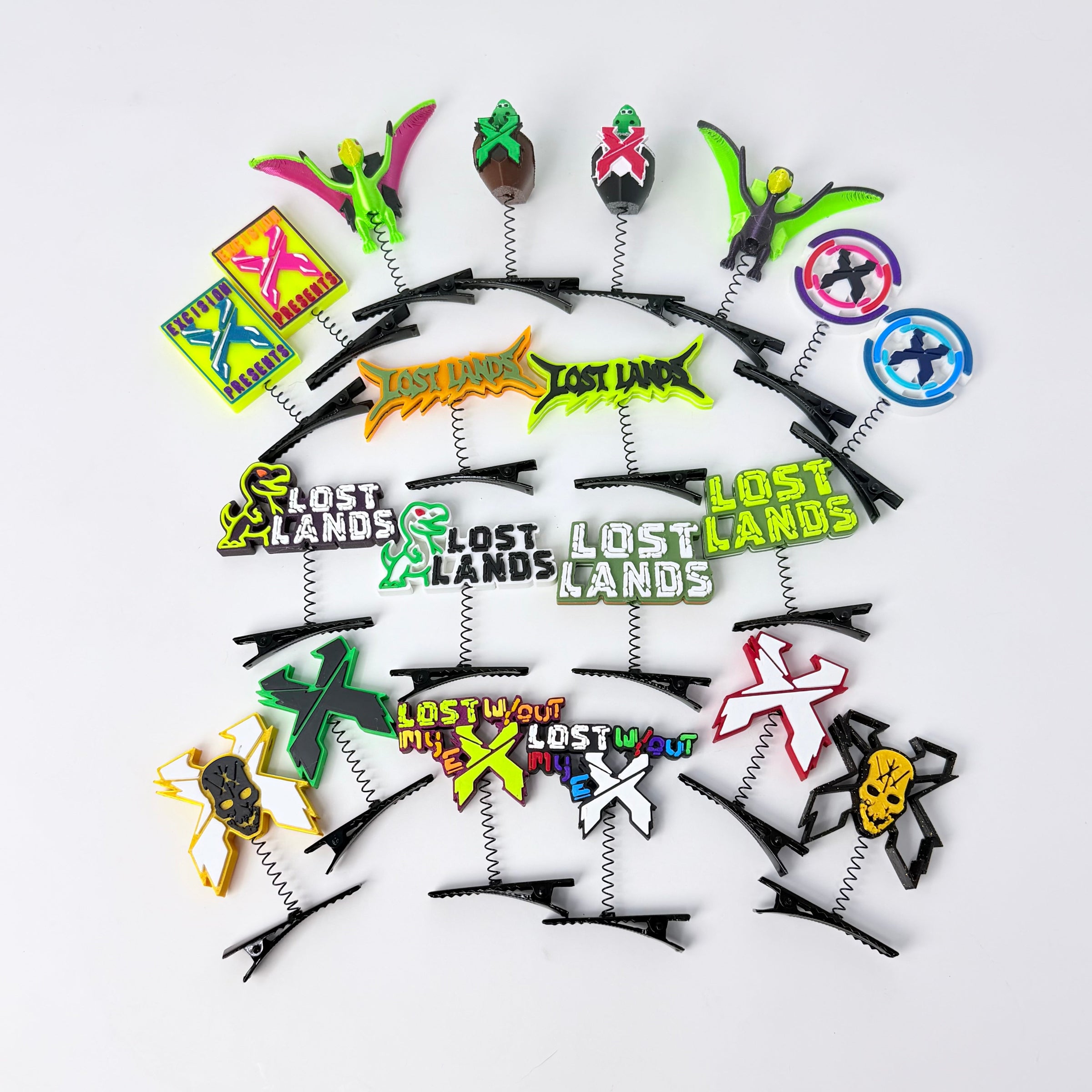 A set of spring hair clips featuring various colorful designs, including the 'Lost Lands' logo, the 'X' key, a skull, and other cartoon motifs, arranged on a plain white background.