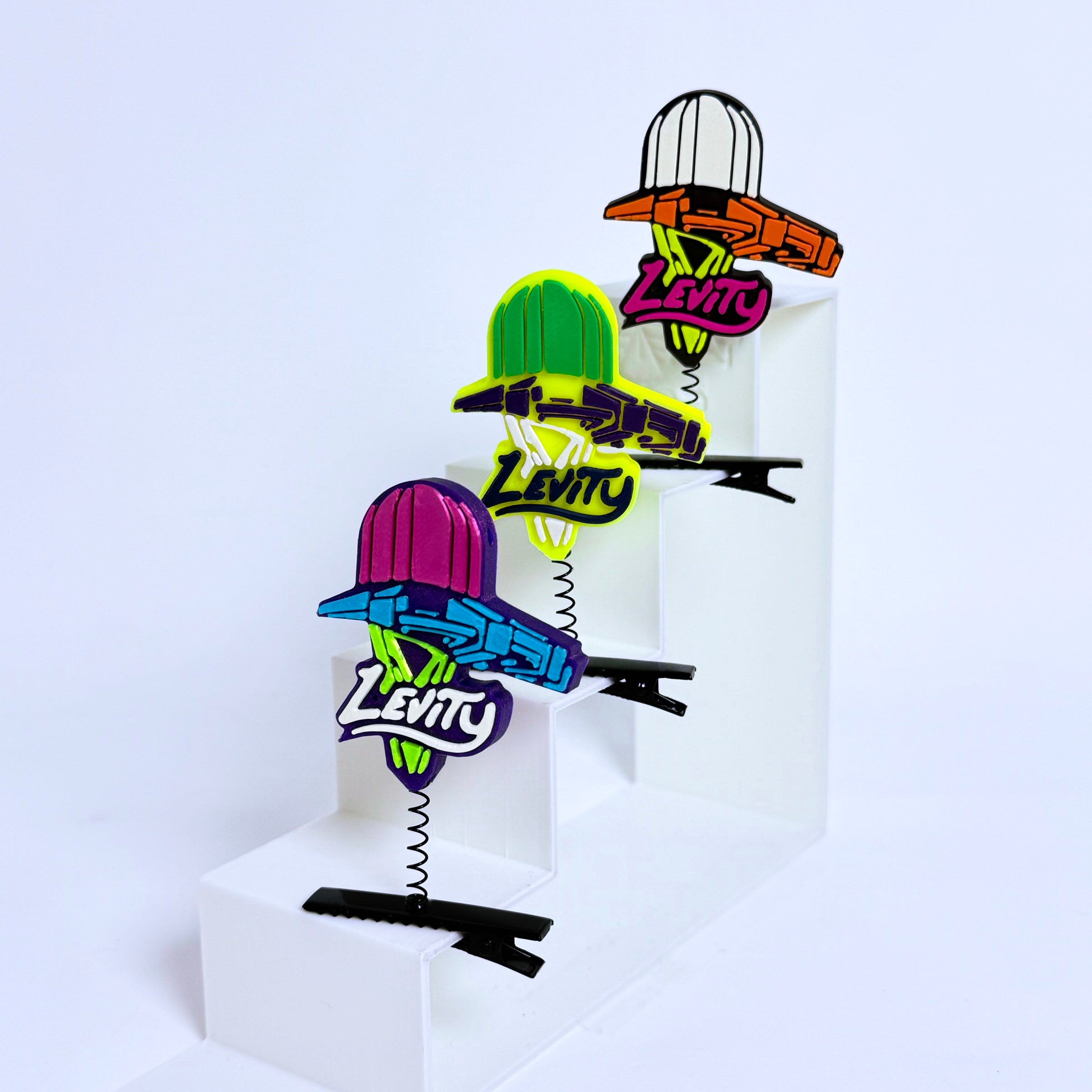 Four fan-inspired Levity Lasership rave sprouts in yellow, purple, black, and multi-color displayed on white risers — EDM festival hair clip accessories with spring clips