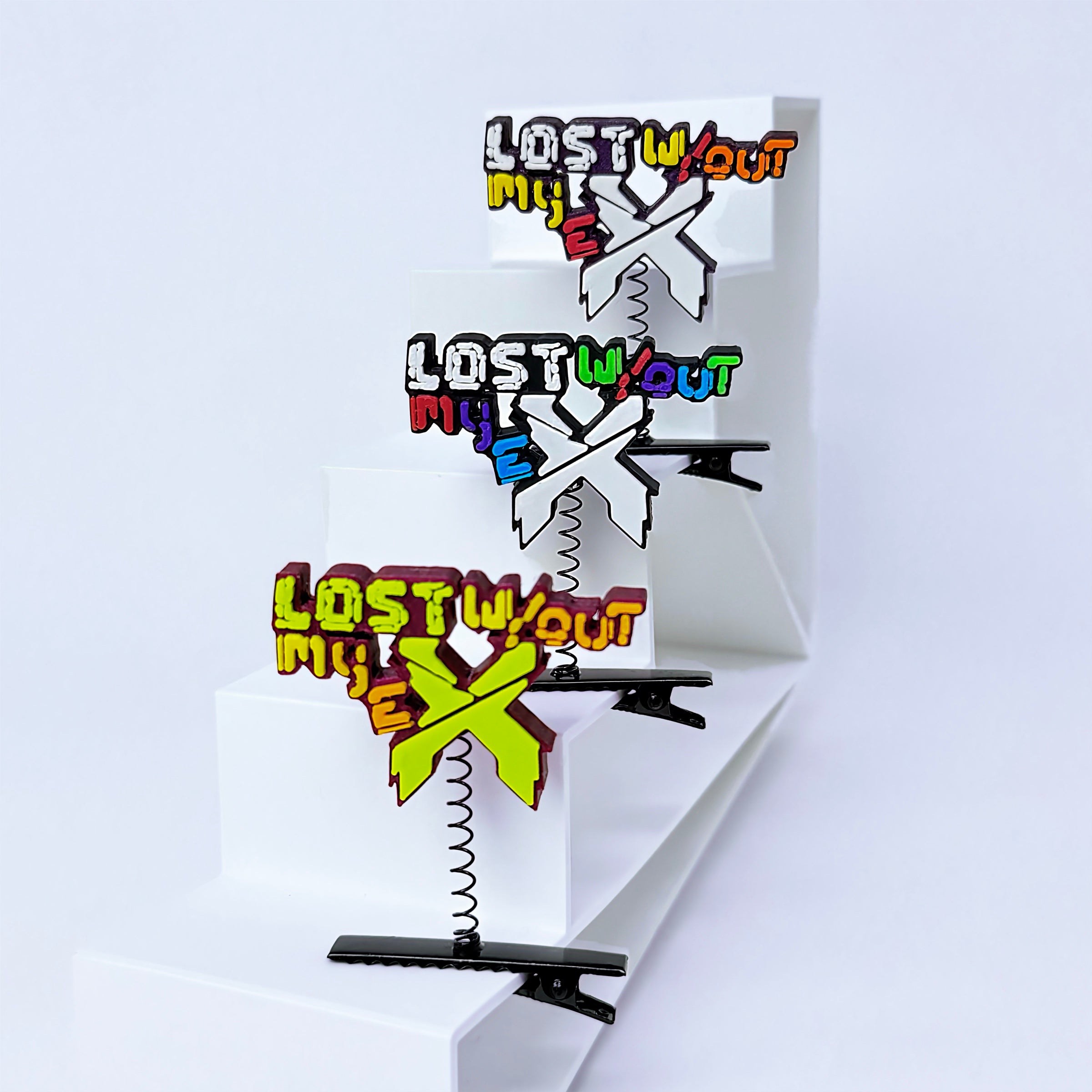 Three rave sprouts with the text 'LOST W/out MY E' and colorful X-shaped charms, displayed on white risers against a white background.