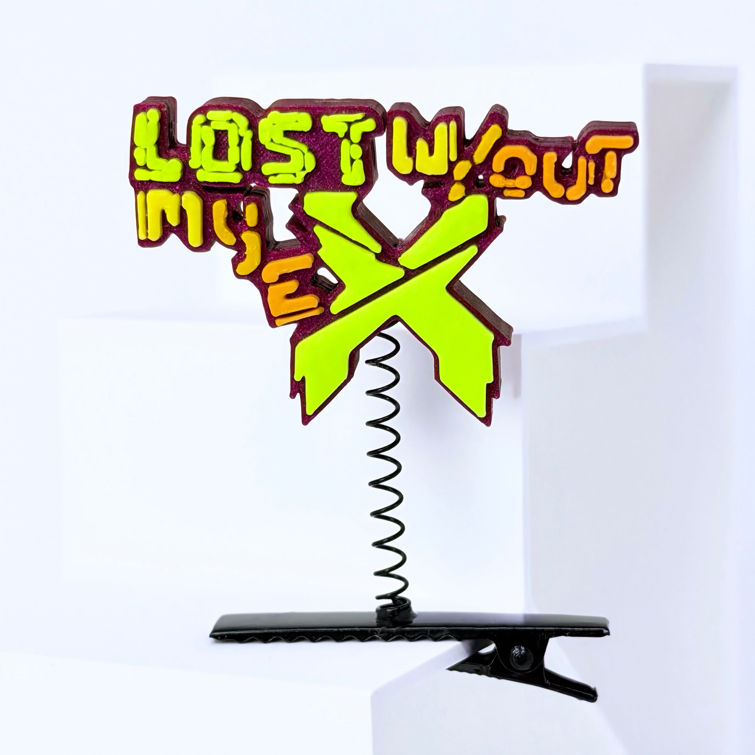 A novelty hair clip standee featuring the 'Lost: The Final Chapter' logo with a bright lime green 'X' and yellow-and-orange 3D lettering, mounted on a black spring and black clip base.